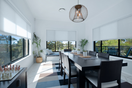 Light-filtering honeycomb blinds fitted to the windows of a bright modern dining room.